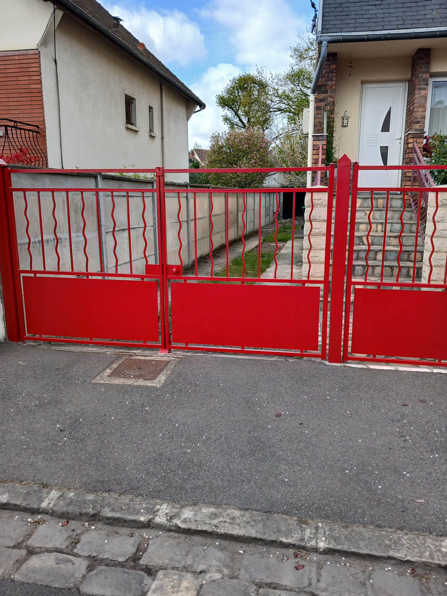 renovation cloture fer Entreprise BAUD Red decorative gate spans the view blocking the narrow driveway between two houses